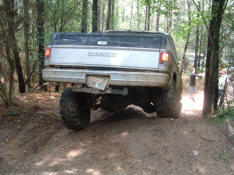 1993 Ford Bronco - Lifted Chevrolet pickup truck navigates a muddy off-road course in the woods.