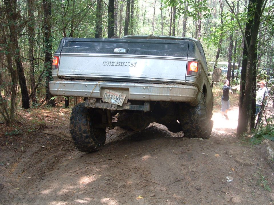 Rear view of lifted Chevrolet pickup truck on muddy trail, with two people watching