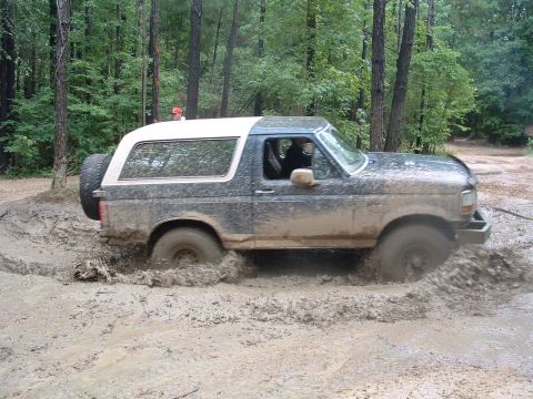 1993 Ford Bronco - A muddy 1993 Ford Bronco navigates a challenging off-road course, splashing through deep mud.