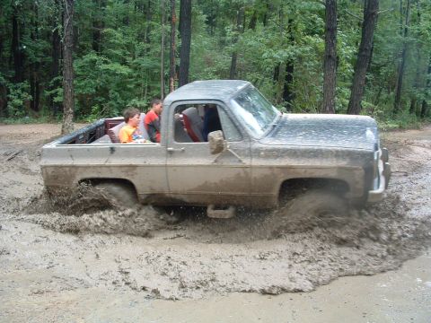1993 Ford Bronco - Kids ride in an old pickup truck as it powers through a muddy trail.