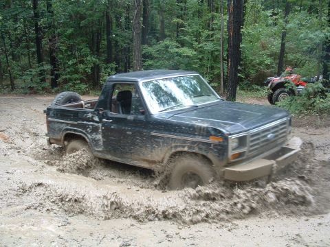 1993 Ford Bronco - A black Ford Bronco II navigates through a muddy trail with an ATV visible in the wooded background.
