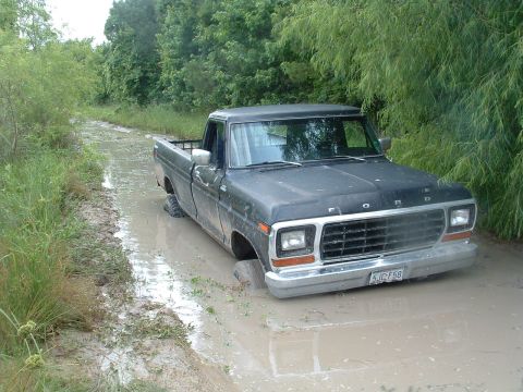 1993 Ford Bronco - Ford pickup truck stuck in mud on a dirt track, with trees and vegetation on either side.