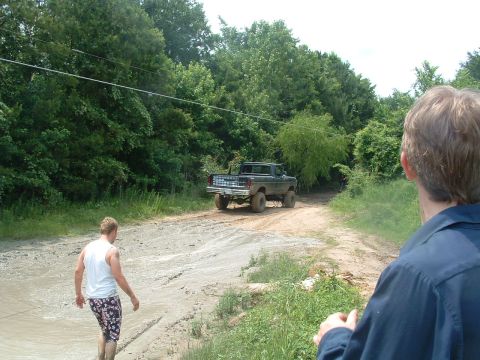 1993 Ford Bronco - Ford F-Series pickup truck navigates a muddy off-road trail with two onlookers present.