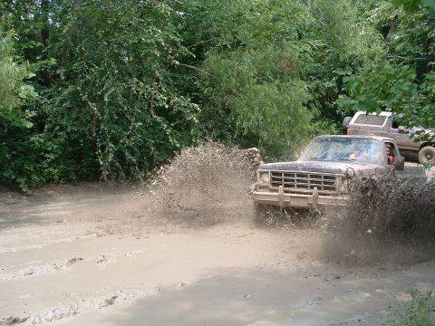 1993 Ford Bronco - Trucks splashing through mud on a trail.
