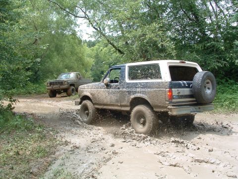 1993 Ford Bronco - A pair of off-road vehicles, a Ford Bronco and a pickup truck, navigate a muddy trail.