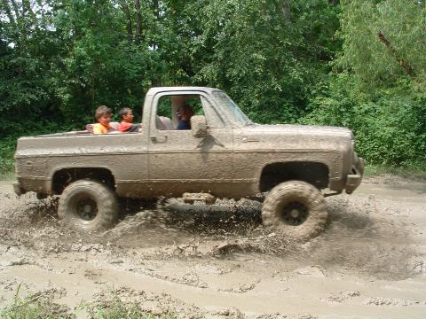 1993 Ford Bronco - Pickup truck splashing through mud with passengers in the cab and bed.
