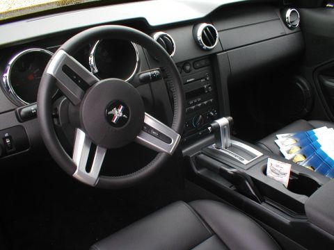 1979 Ford Bronco - The interior of a car, a steering wheel with a Mustang emblem and a center console with an automatic shifter.