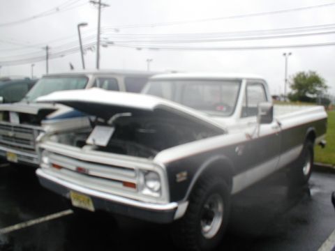 1979 Ford Bronco - A white and black GMC pickup truck is parked with its hood up, next to another vehicle.