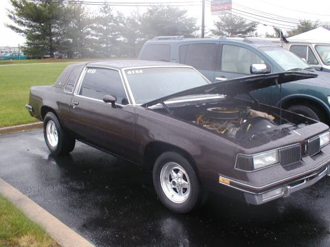 1979 Ford Bronco - A 1981 Oldsmobile Cutlass coupe is parked outside with its hood open, next to a dark green SUV.