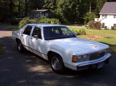 1991 Ford LTD Crown Victoria - A white sedan is parked in a residential driveway on a sunny day.