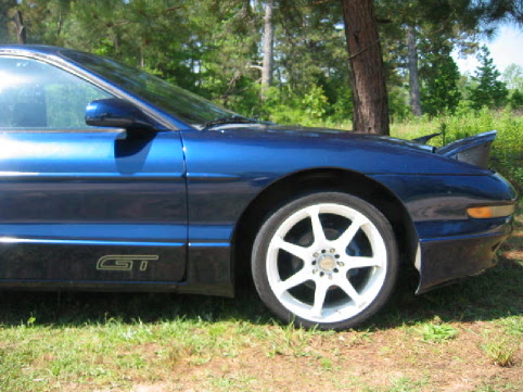 Dark blue Ford Probe GT side view with white seven-spoke wheels, parked on grass