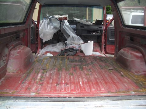 1981 Ford Bronco - The interior of a red SUV is shown, with the cargo area and dashboard covered in protective plastic sheeting.