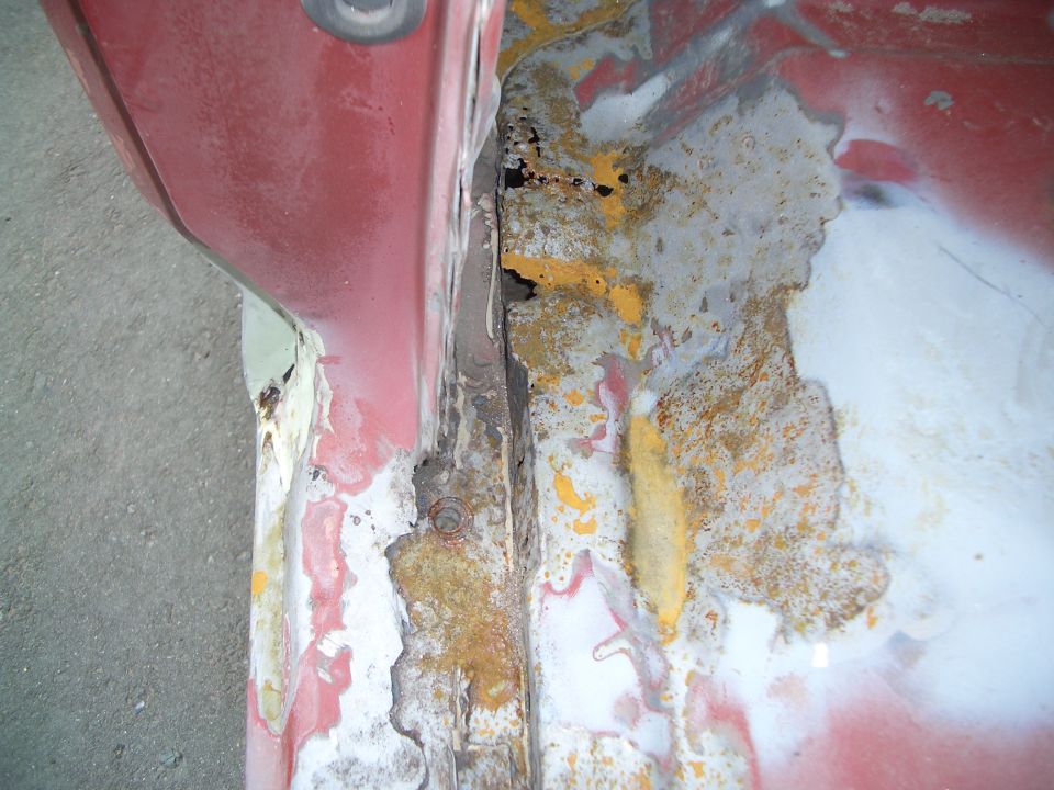 Close-up of a red metal panel with significant rust and peeling paint, showing exposed metal and primer
