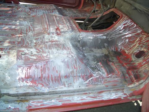 1981 Ford Bronco - The interior floor pan of a vehicle is shown stripped down and prepared for bodywork, revealing the red primer beneath.