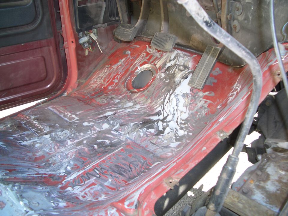 Red interior floor with exposed metal and white residue, showing pedals and door frame