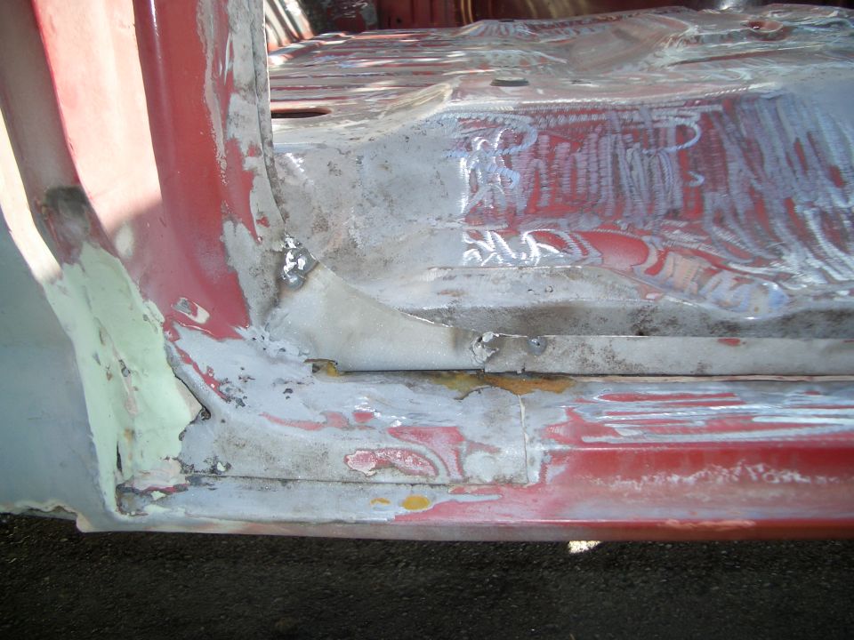 Rusty lower cab corner and rocker with sanded red paint and bare metal during bodywork