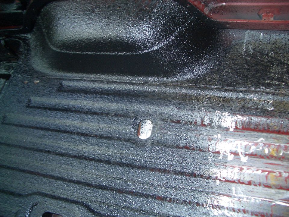 Black textured bedliner coating on ribbed metal floor panel with drain plug and red edge