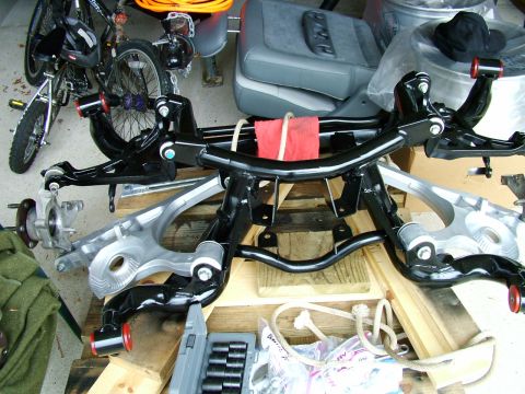 2003 Ford Mustang - Various car suspension parts are arranged on a wooden surface, with a bicycle and car seat visible in the background.