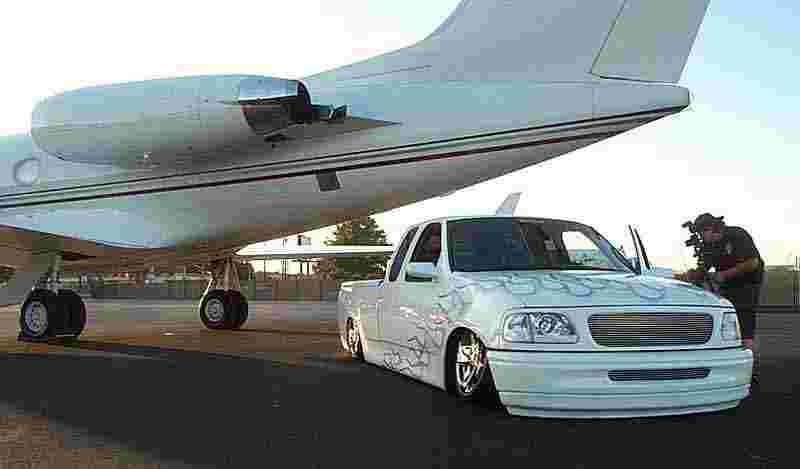 White lowered Ford pickup with flames parked beside a private jet on a tarmac