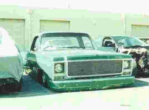 1990 Ford Bronco - green lowered square-body Chevrolet pickup with a billet grille sits in front of pale green warehouse bay doors.
