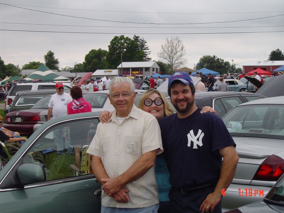 Three people stand in front of a green car at an outdoor car show