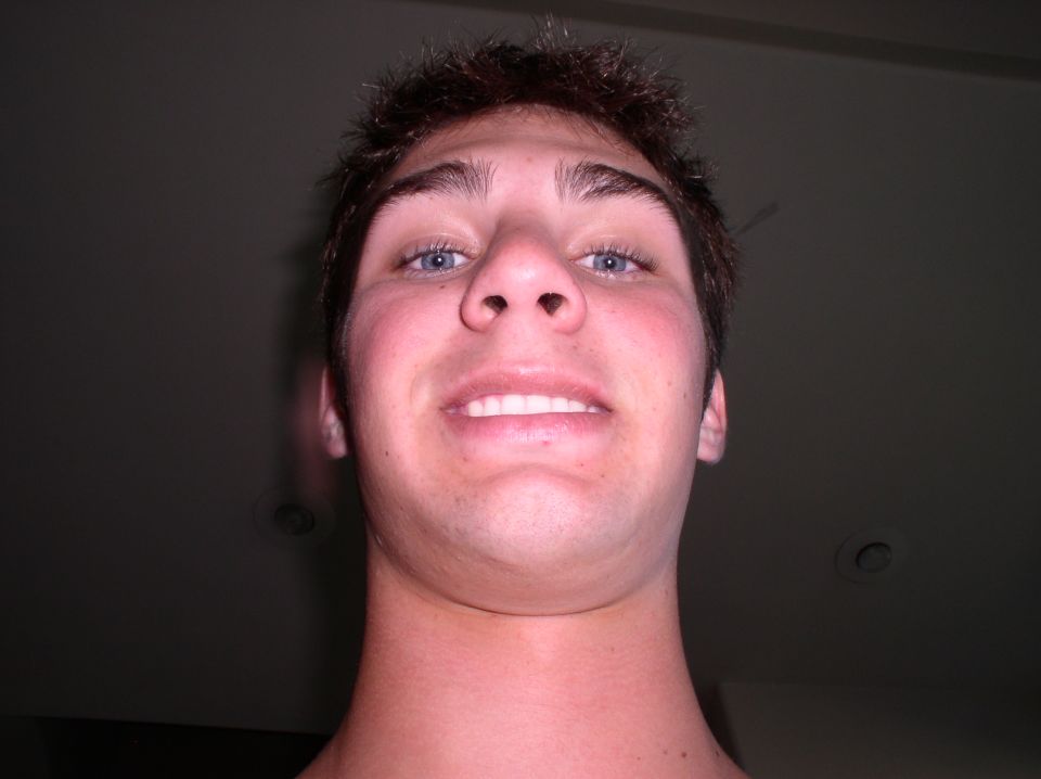 Young man looking up at the camera, smiling with teeth showing. Watermark at bottom right