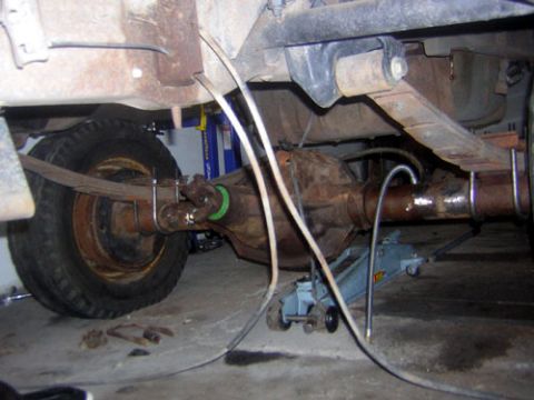 1995 Ford Bronco - Underside shot of a rusty solid rear axle housing with the driveshaft and U-joint bolted at the pinion, one axle end supported on a blue fl…