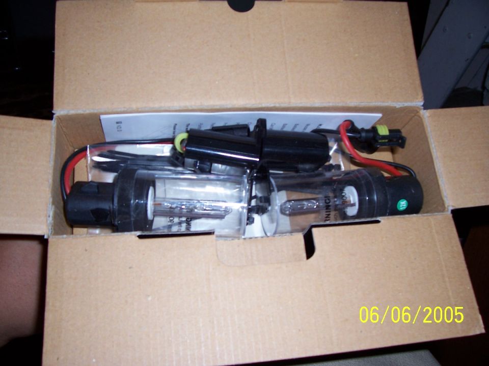 Two HID bulbs with black connectors and wires in a cardboard box
