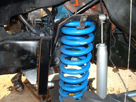 1995 Ford Bronco - The vehicle's front suspension features bright blue coil springs and a silver shock absorber, with visible engine components in the backgro…