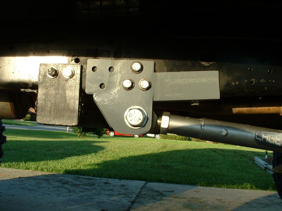 Underside bracket and tie-rod linkage bolted to vehicle frame over grass