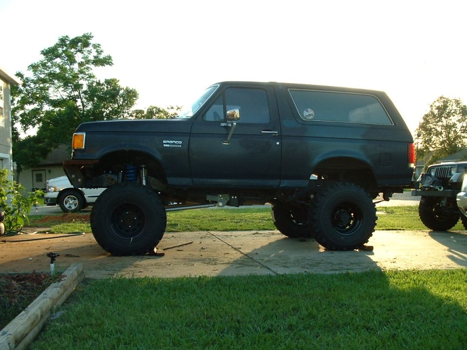 Side view of a lifted dark Ford Bronco SUV on large off-road tires in a driveway