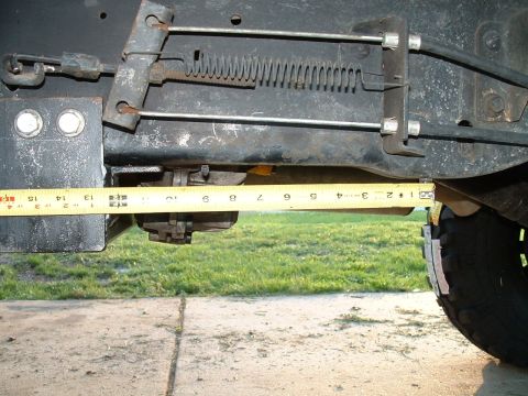 1995 Ford Bronco - A yellow measuring tape is positioned against the underside of a vehicle's frame, showing suspension parts and a tire.