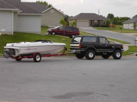 1991 Ford Bronco - Black 1991 Ford Bronco is seen towing a boat on a trailer down a residential street.