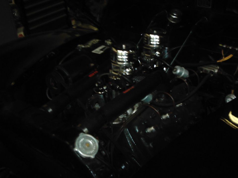 Engine bay with dual chrome carburetors and black valve covers. Radiator cap visible