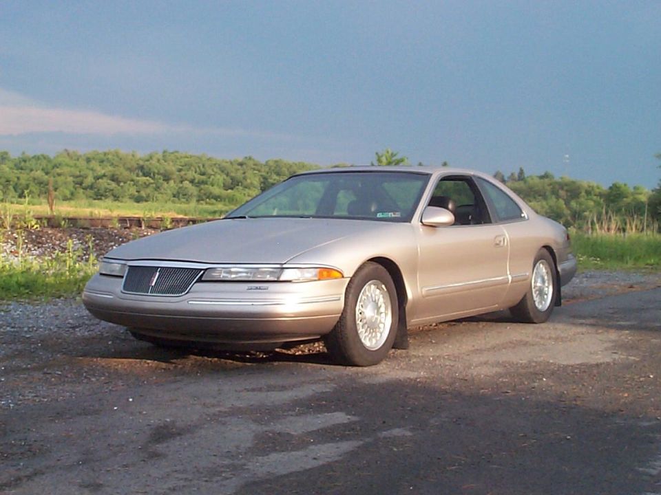 Champagne Lincoln Mark VIII coupe parked on gravel with green hills behind