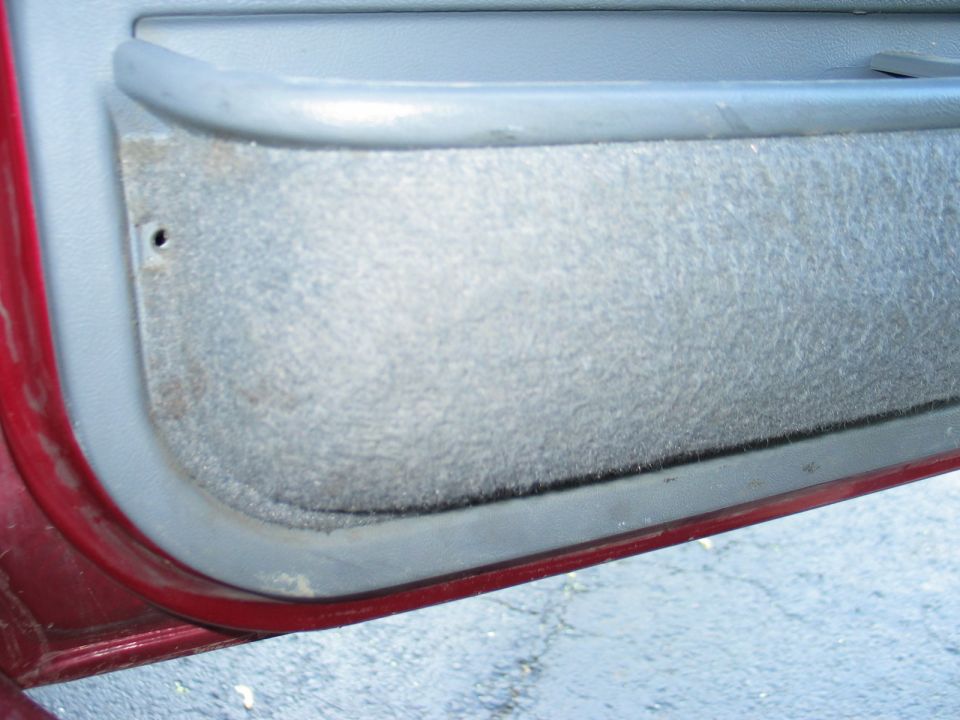 Close-up of a red car's interior door panel with gray fabric insert and pull handle