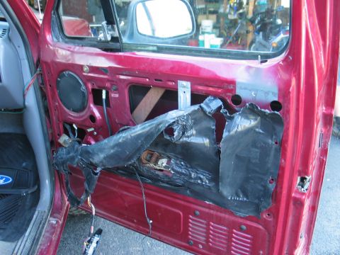 1995 Ford Bronco - The interior of a red car door is visible with the vapor barrier removed, revealing internal components and wiring.