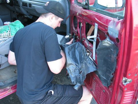 1995 Ford Bronco - A person is kneeling and working on the interior of a red vehicle's door panel.