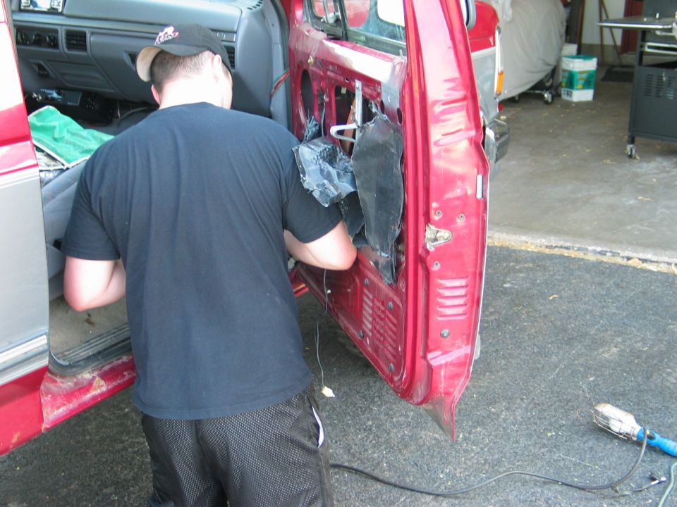 Guy is working on the inside of a red car door, removing the panel. The dashboard is visible inside