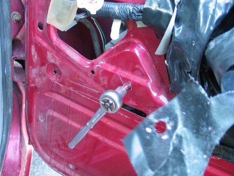 1995 Ford Bronco - Ratchet tool is used to remove a screw from the interior of a red vehicle door panel.