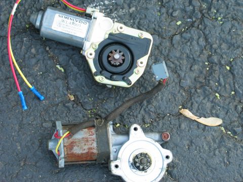 1995 Ford Bronco - Two automotive window motors are shown on a cracked asphalt surface.