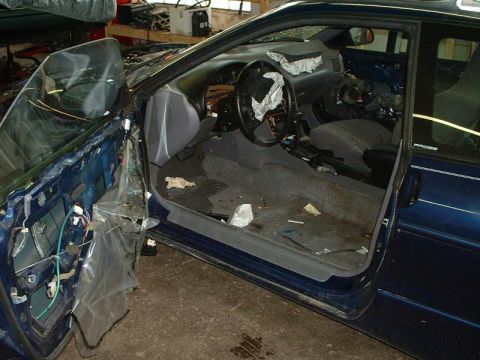 1994 Ford Probe - The interior of a blue car is visible with the driver's side door removed, revealing exposed wiring and a dismantled dashboard.