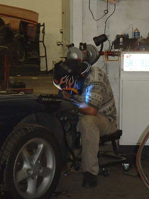 1994 Ford Probe - A person in a welding mask works on the fender of a 1994 Ford Probe, with the front wheel visible.