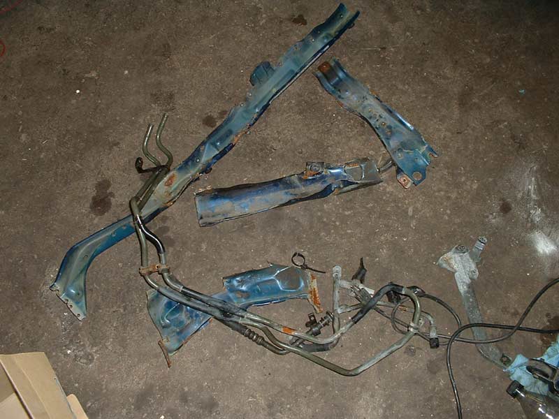 Several blue metal car frame pieces and fuel lines scattered on a concrete floor