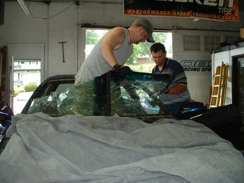 1994 Ford Probe - Two men are removing the shattered windshield from a 1994 Ford Probe inside a garage.