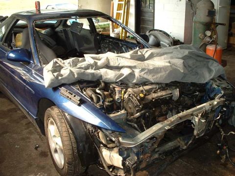 1994 Ford Probe - A blue car sits in a garage with its hood open, revealing the engine and front end damage.