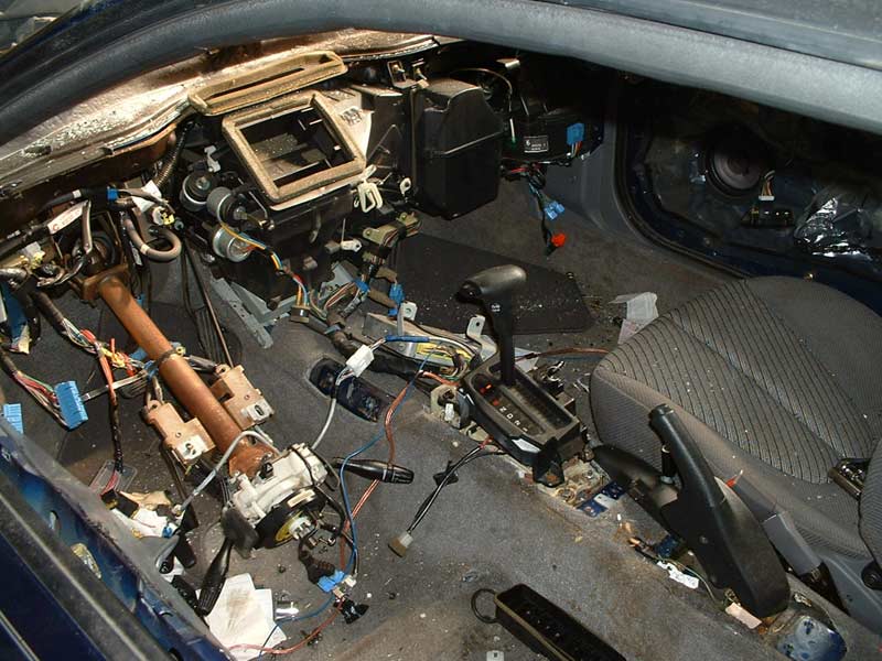 Car interior disassembled, showing dashboard and center console components removed. Wires and parts are exposed
