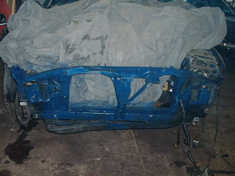 Blue painted car frame with wiring, covered by a grey tarp