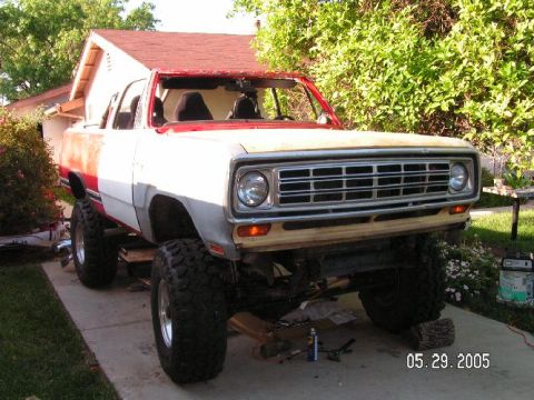 1988 Ford Bronco - A lifted pickup truck sits on a driveway, missing its windshield and undergoing repairs.