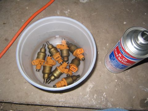 1994 Ford Bronco - Fuel injectors are soaking in a cleaning solution next to a can of automotive cleaner.